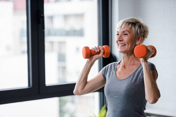 Senior woman lifting dumbbells Active good looking elderly woman smiling and holding dumbbells while working out indoors weight training stock pictures, royalty-free photos & images