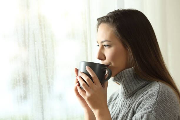 istock Happy woman drinking coffee looking rain through a window 1070148446