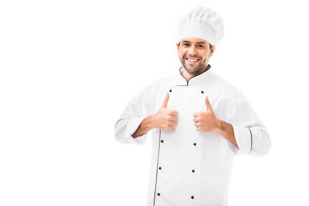 istock handsome young chef showing thumbs up at camera isolated on white 1070151580