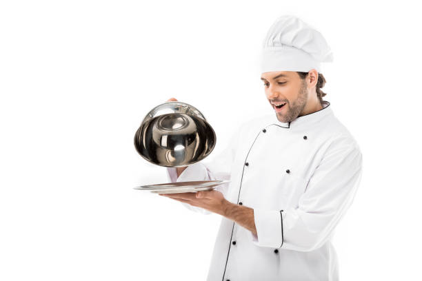 istock surprised young chef taking of serving dome from plate isolated on white 1070153122