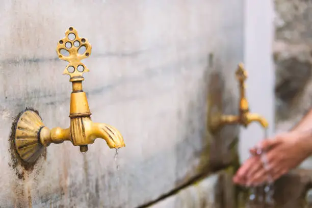 Two old public taps in Istanbul, Turkey. Water flowing and person washing hands in background.