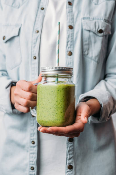 istock Female hands holding glass jar with green nutritious smoothie and straw 1070161628