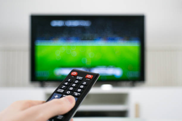 istock Hand holding TV remote control in front of blurred TV background 1070162404