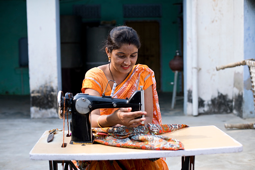 Happy Indian woman sewing clothes with sewing machine