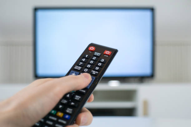 istock Hand holding TV remote control in front of blurred TV background 1070163132
