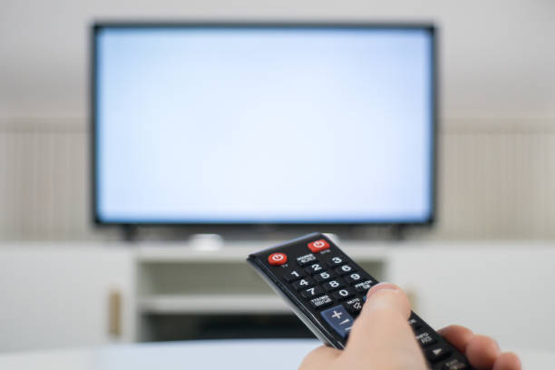 istock Hand holding TV remote control in front of blurred TV background 1070164790