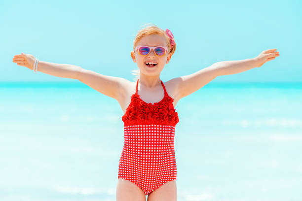 istock happy modern child in red swimsuit on seashore rejoicing 1070178628