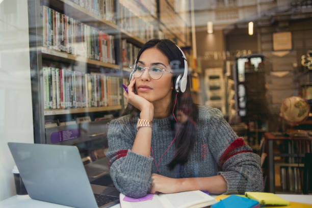 jovem mulher a trabalhar em seu laptop na biblioteca - using computer audio - fotografias e filmes do acervo