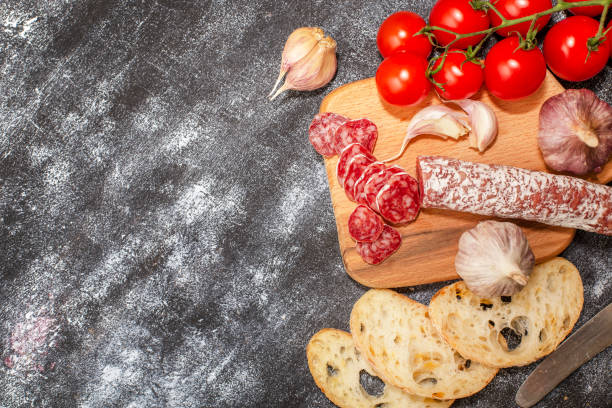 istock Salami sausage with tomatoes and garlic on a cutting board. Top view with copy space on dark background 1070187764