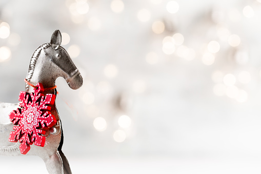 Christmas silver vintage horse with red wooden snowflake on neck against festive bokeh background, new year celebration greeting card, copy space