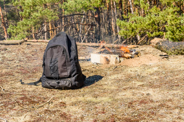 istock Backpack on a ground in a coniferous forest. Bonfire on a background 1070207606