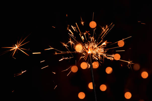 istock Macro, close up. Bright burning sparkler with flying sparks. Dark background with blurred lights of Christmas garland. 1070215352