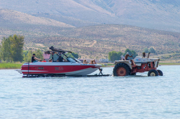 Boat Farmer on a Tractor Pulling Motorboat Into Bear Lake I saw this during our trip to Bear Lake in Idaho.  Boat rental places are scattered all around the lake.  This one did not have a dock or launch so they used a couple of tractors to pull the boats on a trailer into deep water.  The boat is jam packed with a large extended family with all the girls up in front.  I did not stay long enough to find out how the boat returns to shore and whether all the passengers have to swim or wade in or if the tractor will go out and pick them up again. ursus tractor stock pictures, royalty-free photos & images