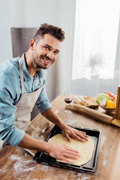 istock smiling young man in apron preparing pizza dough on baking tray 1070231494