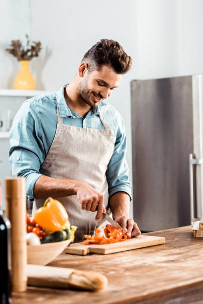 istock smiling young man in apron chopping fresh vegetables in kitchen 1070232280