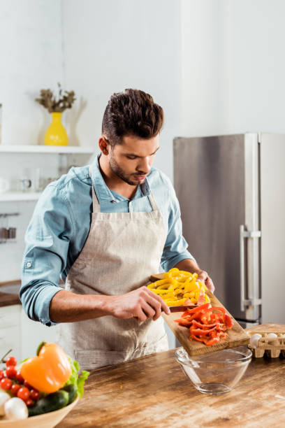 istock handsome young man in apron preparing vegetable salad in kitchen 1070232486