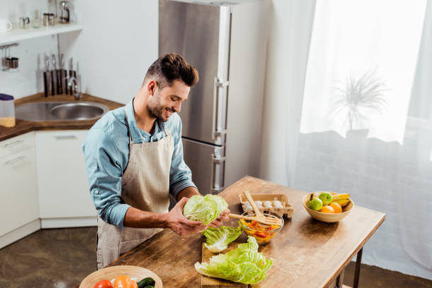 istock high angle view of smiling young man in apron holding fresh cabbage in kitchen 1070232736