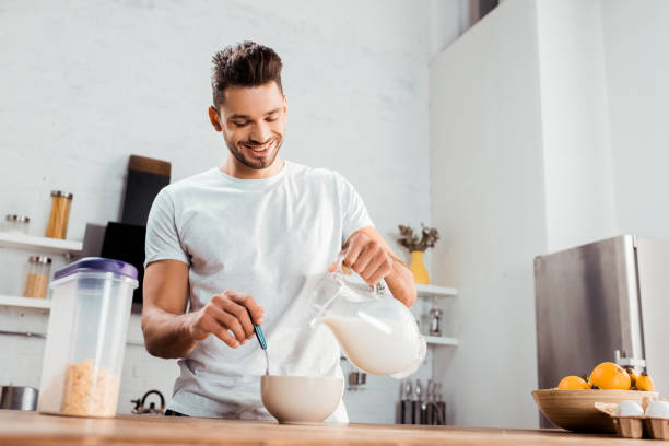 istock smiling young man pouring milk into bowl with corn flakes 1070241302