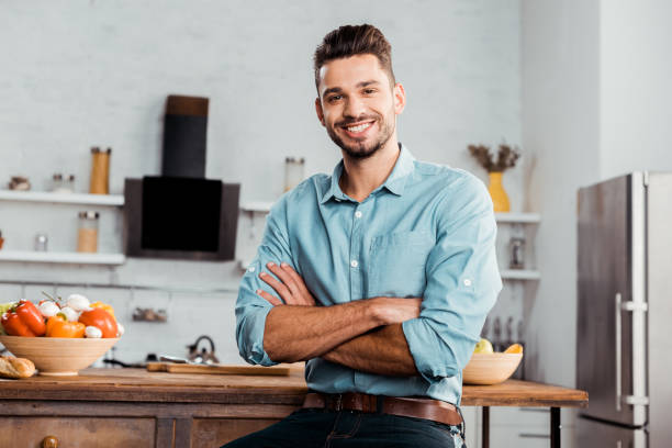 istock handsome young man with crossed arms smiling at camera in kitchen 1070243026