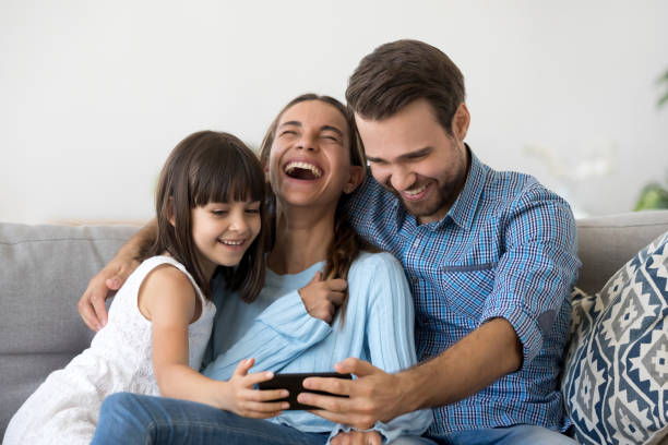 istock Family sitting on couch using smartphone watching video laughing 1070261810