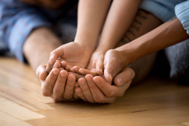 famiglia sdraiata sul pavimento insieme che si tiene per mano - multi generation family adoption family human hand foto e immagini stock