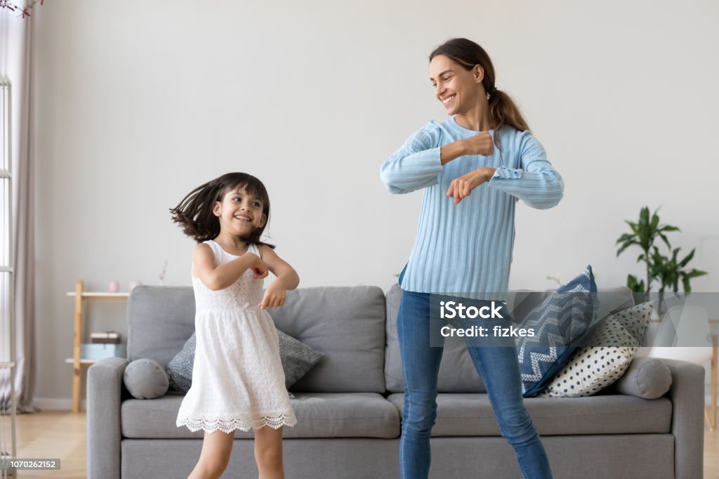 Mother and daughter dancing together in living room Cheerful mother little daughter standing in living room at home moving dancing to favourite song together. Child have fun with elder sister nanny or loving mother active leisure and lifestyle concept Dancing Stock Photo