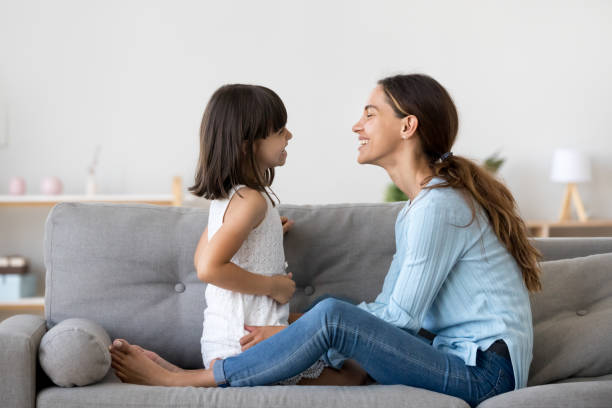 Mother spend time with little daughter talking sitting on couch