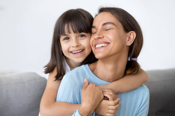 istock Laughing mother and daughter hugging sitting on sofa 1070267282