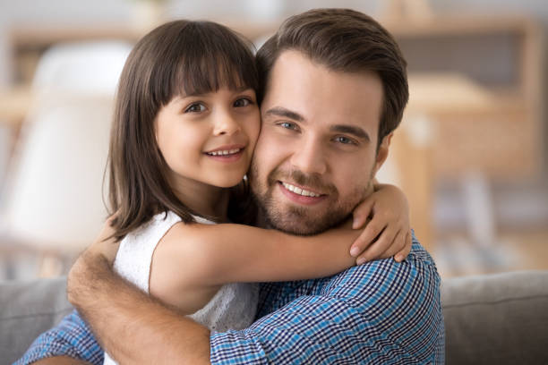 istock Father and daughter embracing sitting on couch looking at camera 1070267348