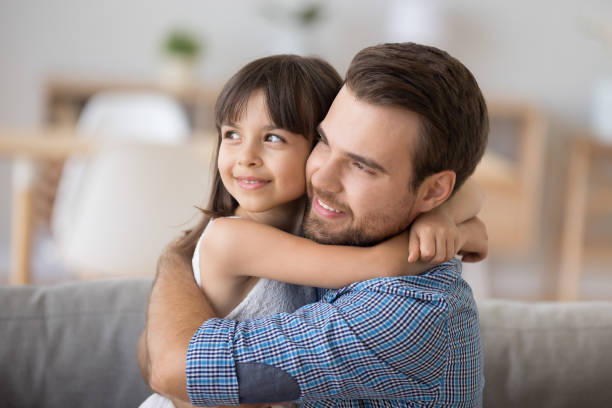 istock Father and daughter embracing sitting on couch looking at camera 1070267364