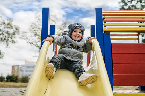 Close Up portrait of Boy Sliding down the slide in Park in Autumn day. Cold, Winter, smiling, having fun