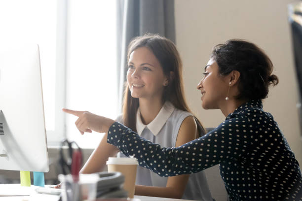 szczęśliwy kaukaski stażysta słuchający indyjskiego mentora wyjaśniającego zadanie komputerowe - women togetherness teaching laptop zdjęcia i obrazy z banku zdjęć