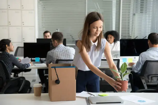 Photo of Smiling hired female company employee unpacking box with personal belongings