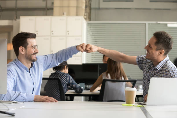Friendly smiling male colleagues fist bumping celebrating good teamwork result Friendly smiling male colleagues fist bumping at workplace celebrating good teamwork result concept, happy coworkers sharing success motivated by collaboration at work, respect or cooperation concept office buddies stock pictures, royalty-free photos & images