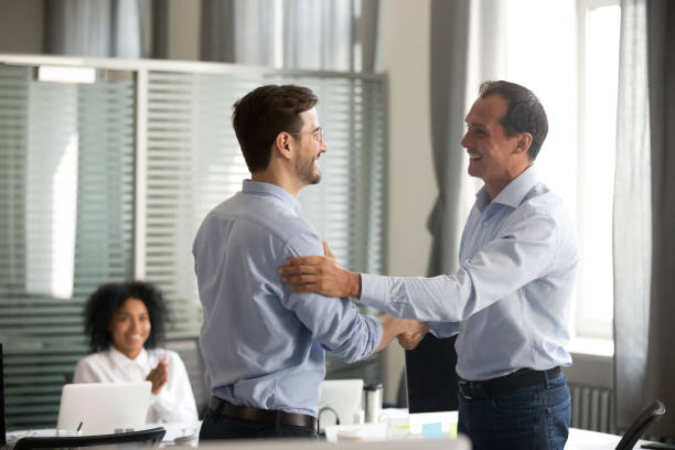Smiling middle-aged ceo handshaking successful male worker showing respect Smiling middle-aged ceo promoting motivating worker shaking hands congratulating with achievement promising respect bonus thanking for good work, team applauding, employee reward recognition concept encouragement photos stock pictures, royalty-free photos & images