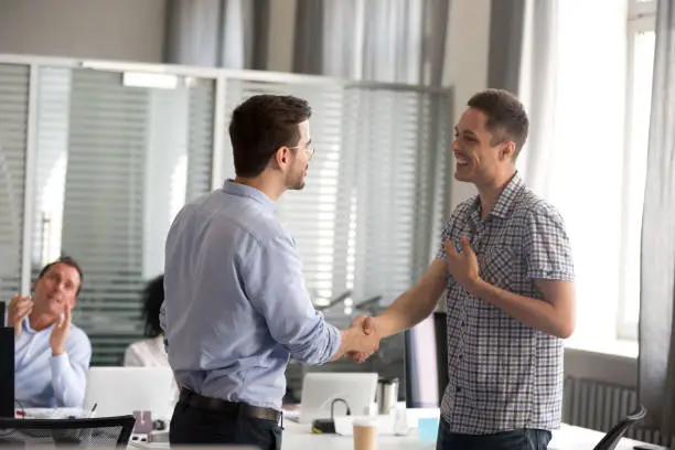 Photo of Ceo motivating rewarding male employee shaking hand congratulating with promotion