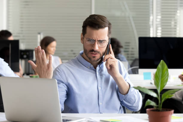 Angry businessman caller talking on phone disputing over computer problem Angry business man talking on phone disputing looking at laptop, stressed frustrated office worker arguing by mobile solving online computer problem with technical support complaining on bad service brat stock pictures, royalty-free photos & images