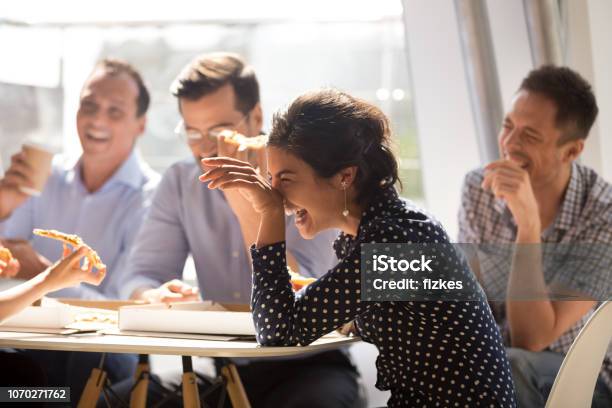 Indian Woman Laughing Eating Pizza With Diverse Coworkers In Office Stock Photo - Download Image Now