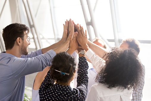 Diverse business team associates office workers group giving high five together as concept of coaching, teamwork involvement, engaging in teambuilding, motivated by unity, good corporate relations