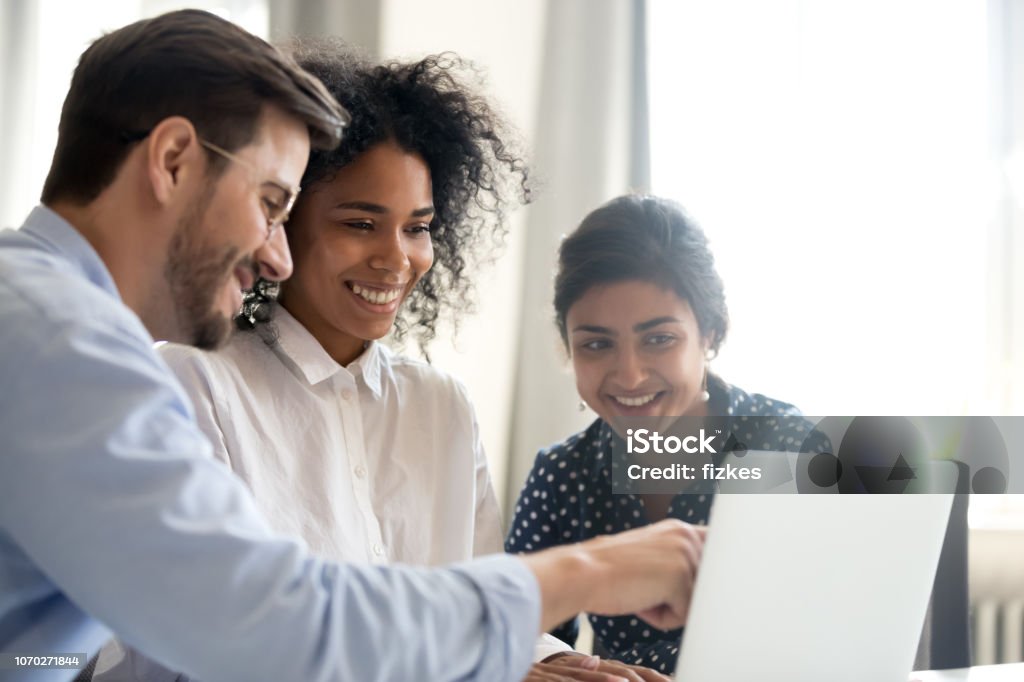 Diverse happy interns listening to mentor explaining online project Diverse happy interns learning new computer software listening to mentor teacher coach teaching explaining online project application on laptop, smiling multi-ethnic coworkers work together in office Teamwork Stock Photo