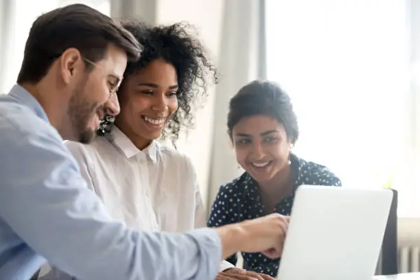 Photo of Diverse happy interns listening to mentor explaining online project