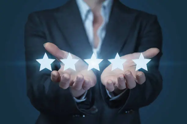 Photo of A businesswoman is holding a line of golden shining stars at the dark background.