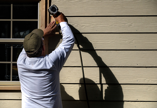 Carpenter using a nail gun to install siding on a home.