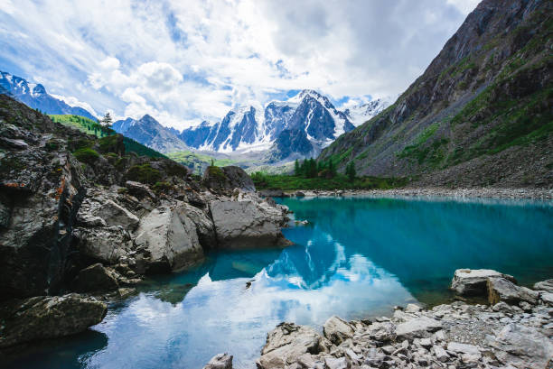 Mountain lake is surrounded by large stones and boulders on front of giant beautiful glacier. Amazing snowy mountains. Ridge with snow. Wonderful atmospheric landscape of majestic nature of highlands. lago de la montaña está rodeada de grandes piedras y rocas en frente del gigantesco glaciar hermoso. impresionantes montañas nevadas. arista de nieve. maravilloso paisaje atmosférico de la majestuosidad de la naturaleza de las tierras altas.