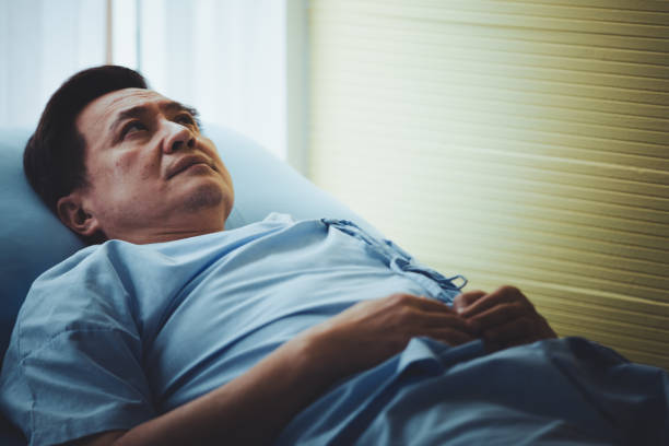 Patient senior man lying on bed resting tired looking sad stock photo