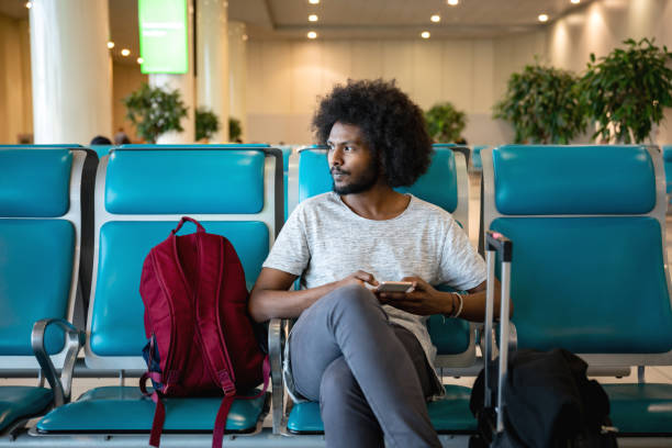 mâle voyageur à l’aéroport à l’aide de son téléphone portable en attendant son vol - arrival airport airport lounge flying photos et images de collection
