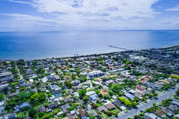 Aerial view of residential area near ocean coastline and long wooden pier with sailboats.