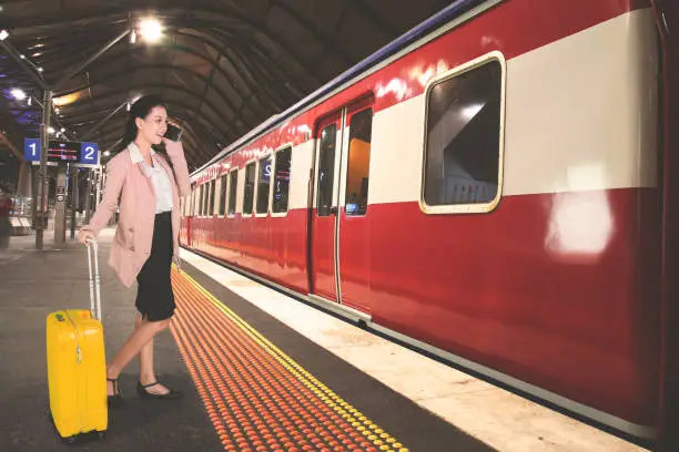 Picture of Caucasian businesswoman speaking on a mobile phone while holding a suitcase in the train station