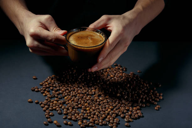 cup of hot coffee in the hands with scattered roasted grains on the table - fotografia de stock