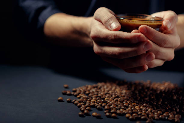 cup of hot coffee in the hands with scattered roasted grains on the table - fotografia de stock